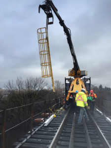 boom lowering cage ladder into place on bridge repair site